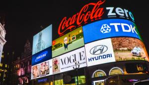 Color photo of multiple neon signs featuring brand logos affixed to a building