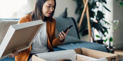 Person looking at a new clothing purchase in a box while holding a phone