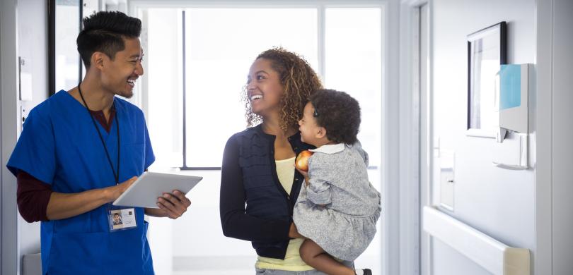 Man in blue scrubs speaking in hallway of medical building with mother and small child