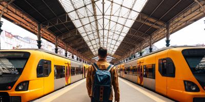 Color photo of man with backpack at a train station facing two trains