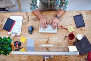 Overhead view of person at desk typing on wireless keyboard with office supplies and coffee mugs