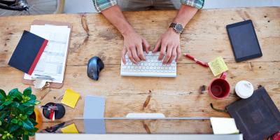 Overhead view of person at desk typing on wireless keyboard with office supplies and coffee mugs