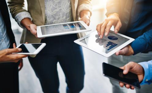 Four people standing with phones and tablets in hands with data charts on screens