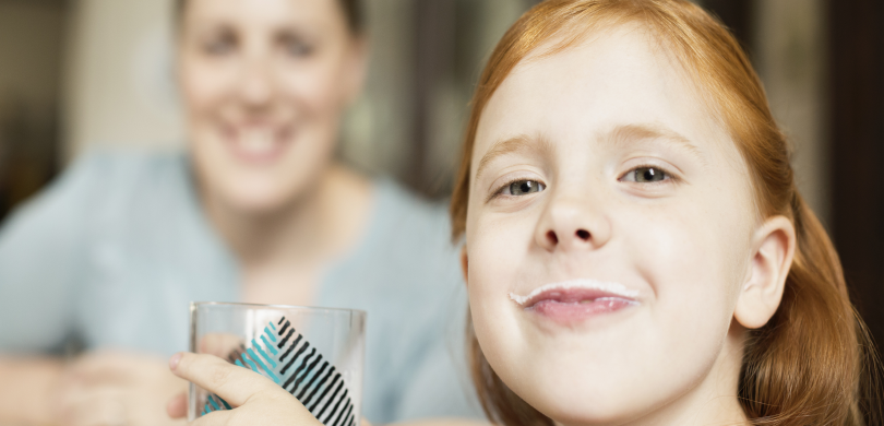 Girl with milk mustache with mother in background