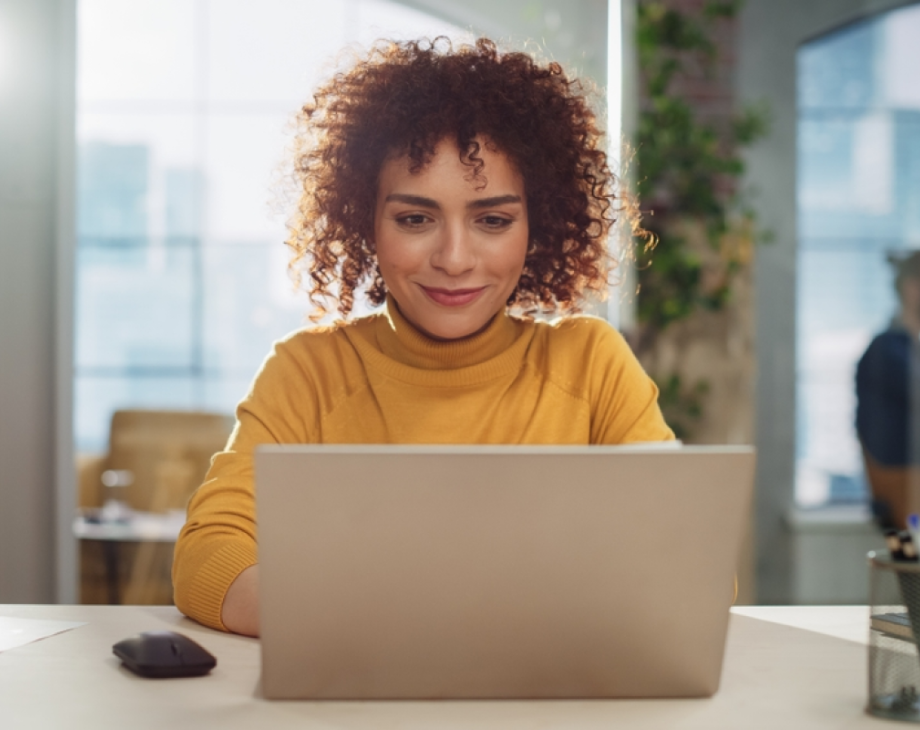 Photo of woman of color facing the camera and typing on a laptop