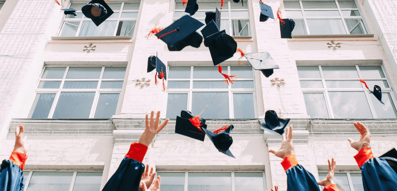 College graduates throwing black and orange caps into the air